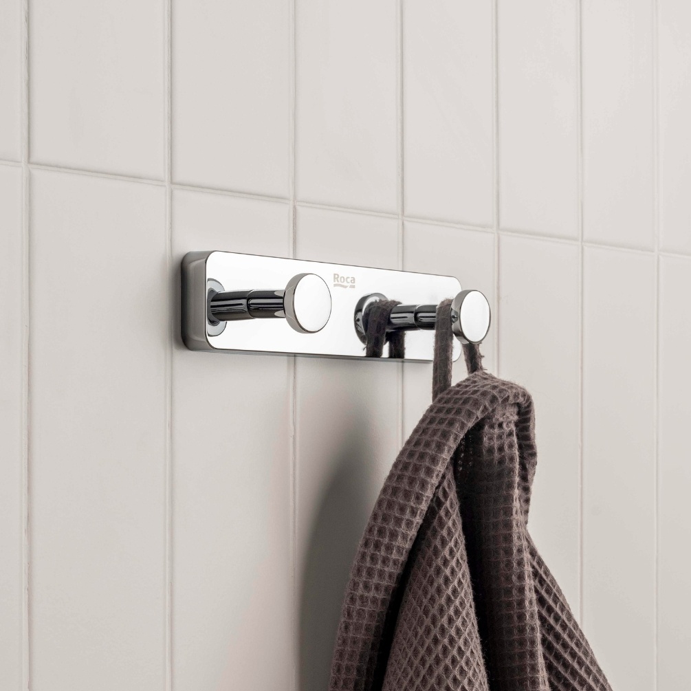 Lifestyle image of the Roca Sonata Chrome Double Robe Hook installed on a bathroom wall and hanging a brown robe